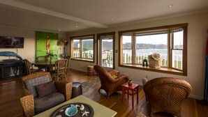 A spacious living room with large windows, wicker furniture, a television, and a view of the water. - MENDO VILLAGE LUXURY OCEANFRONT PENTHOUSE, DOG FRIENDLY, VIEWS, WALK EVERYWHERE! (Mendocino)