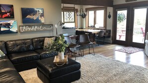 A spacious living room with a black leather sofa, a coffee table with a vase of flowers, and a dining area with a wooden table and chairs. - The Best Alaskan Get Away Retreat For Your Family Or Group (Anchorage)
