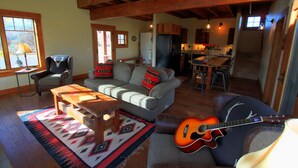 A spacious living room with a high ceiling, a dining area, and a kitchen in the background.