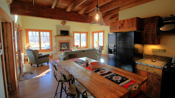 A spacious kitchen with a large island, a stone fireplace, and a refrigerator.