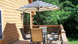 A wooden deck with outdoor furniture, including chairs and a table, and a striped umbrella.