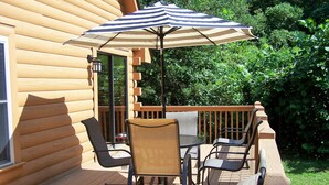 Eine Holzterrasse mit Gartenmöbeln, darunter Stühle und ein Tisch, und einem gestreiften Sonnenschirm.
