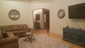 A living room with a brown sofa, a glass coffee table, a patterned rug, a blue cabinet, and a wall-mounted TV.