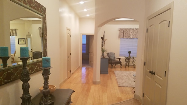 A hallway with a wooden floor, a mirror with a decorative frame, a dresser with a mirror, and a door on the right.