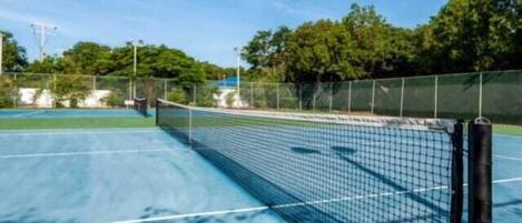 An outdoor tennis court with a net, surrounded by trees and a clear sky.