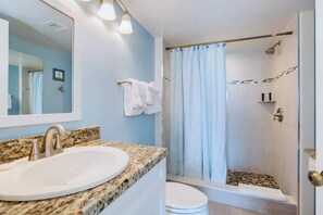 A bathroom with a granite countertop sink, a mirror, a shower with a glass door, and a toilet.