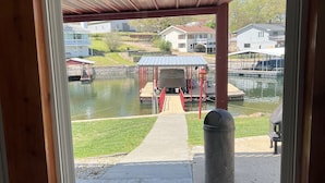 A view through a window of a covered dock area with a boat, a red pavilion, and a pathway leading to a dock.