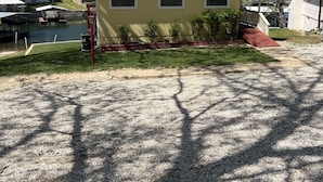 A yellow house with a gravel driveway, a small porch, and a pond in the background.