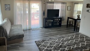 A living room with a sofa, a TV on a stand, a dining table with chairs, and a rug.