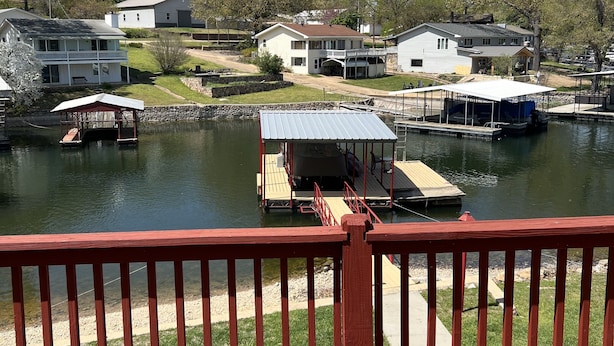 A lakeside view with a wooden deck, docked boats, and houses in the background.