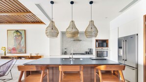 Een moderne keuken met een groot eiland, roestvrijstalen apparatuur en hanglampen.