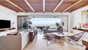 Een moderne woonkamer met een grote bank, twee fauteuils, een televisie en uitzicht op zee.