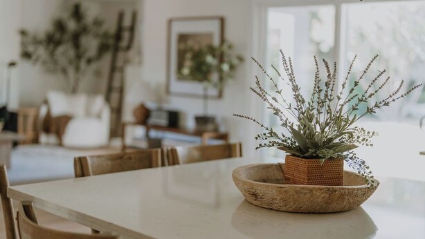 A dining table with a woven bowl containing a plant, surrounded by wooden chairs.