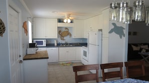 A compact kitchen with white cabinets, a microwave, a refrigerator, and a ceiling fan.