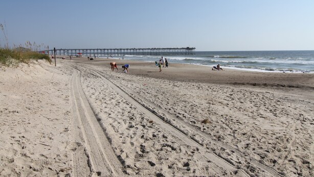 Ein Sandstrand mit einem Pier im Hintergrund.
