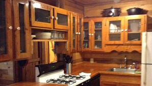 A wooden kitchen with a gas stove, oven, and cabinets. There is a sink and a refrigerator.