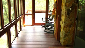 A wooden deck with a rocking chair and a rug.