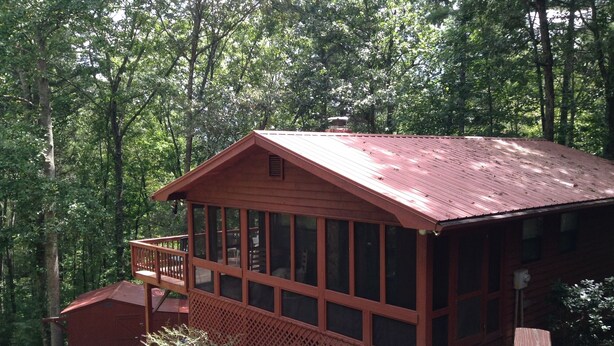 A cabin with a wooden exterior, a deck, and a covered porch.