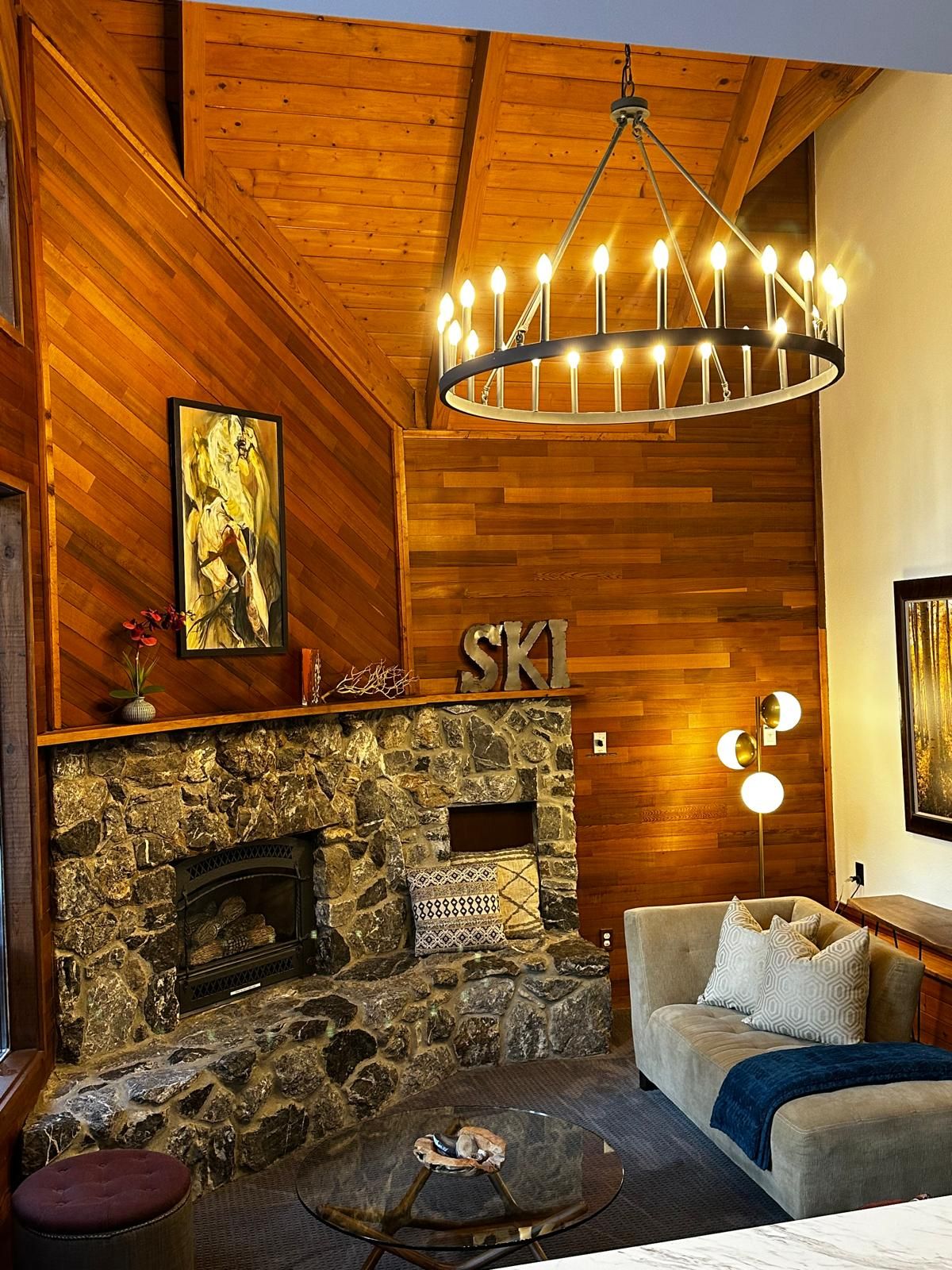 Una habitación acogedora con chimenea de piedra, paredes de madera, un sofá y una araña.