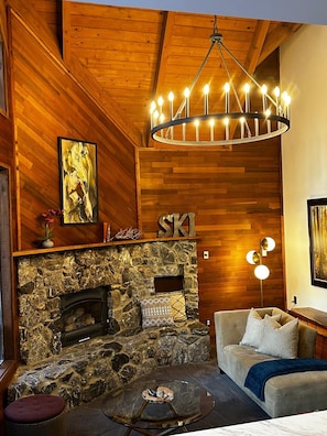 A cozy room with a stone fireplace, wooden walls, a sofa, and a chandelier.