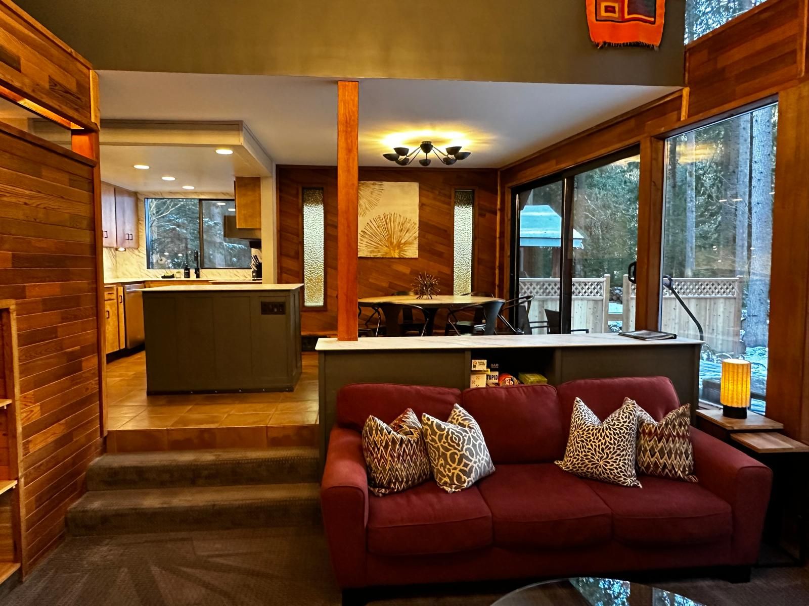 A modern interior with a red sofa, wooden walls, a kitchen area, and large windows.