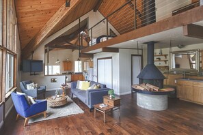 A spacious living area with a high ceiling, wooden beams, a fireplace, and a kitchen in the background. - Charming House Inside the Gate of Sequoia National Park (Three Rivers)
