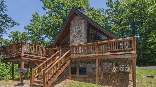 A rustic cabin with a stone chimney, wooden deck, and a staircase leading to a second level. - Cloud Nine: Charming Mountain Cabin, Amazing Views!  Now featuring a new bed! (Sevierville)