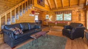 A log cabin interior with a wooden staircase, a black leather sofa, a wooden coffee table, and a pool table. - Cloud Nine: Charming Mountain Cabin, Amazing Views!  Now featuring a new bed! (Sevierville)