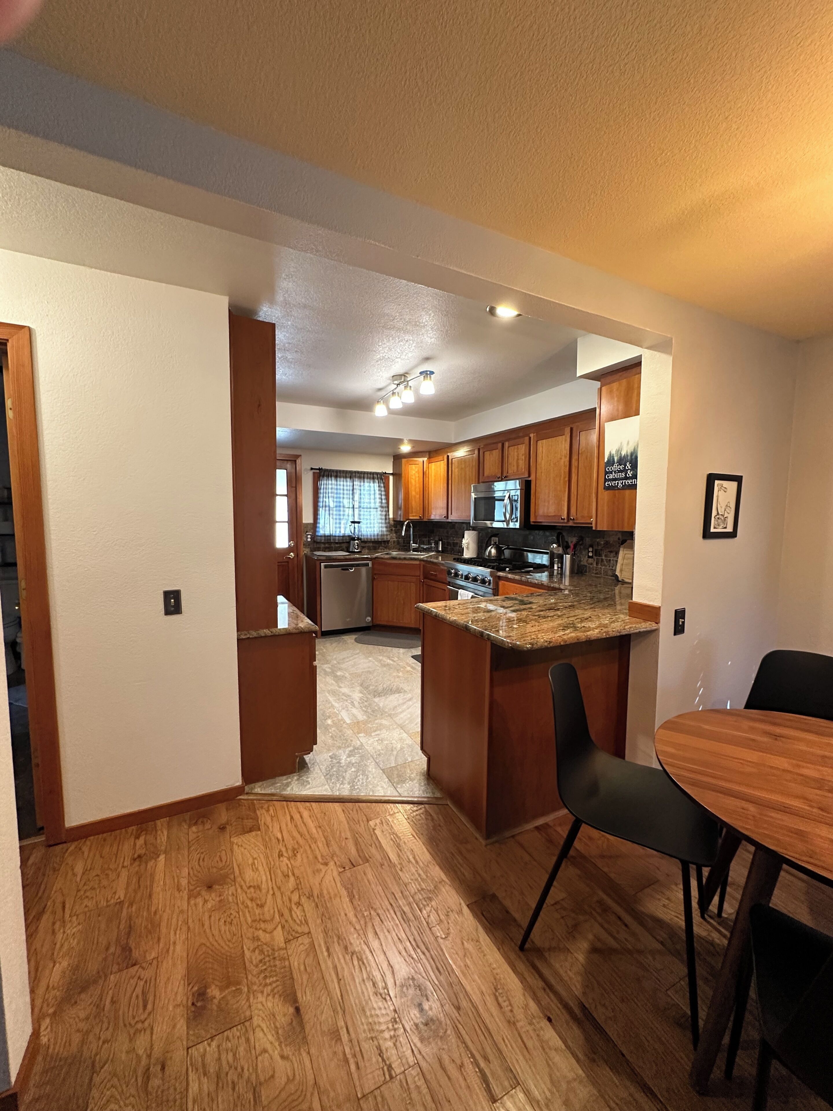 A modern kitchen with wooden cabinets, a granite countertop, and a dining area with a table and chairs.