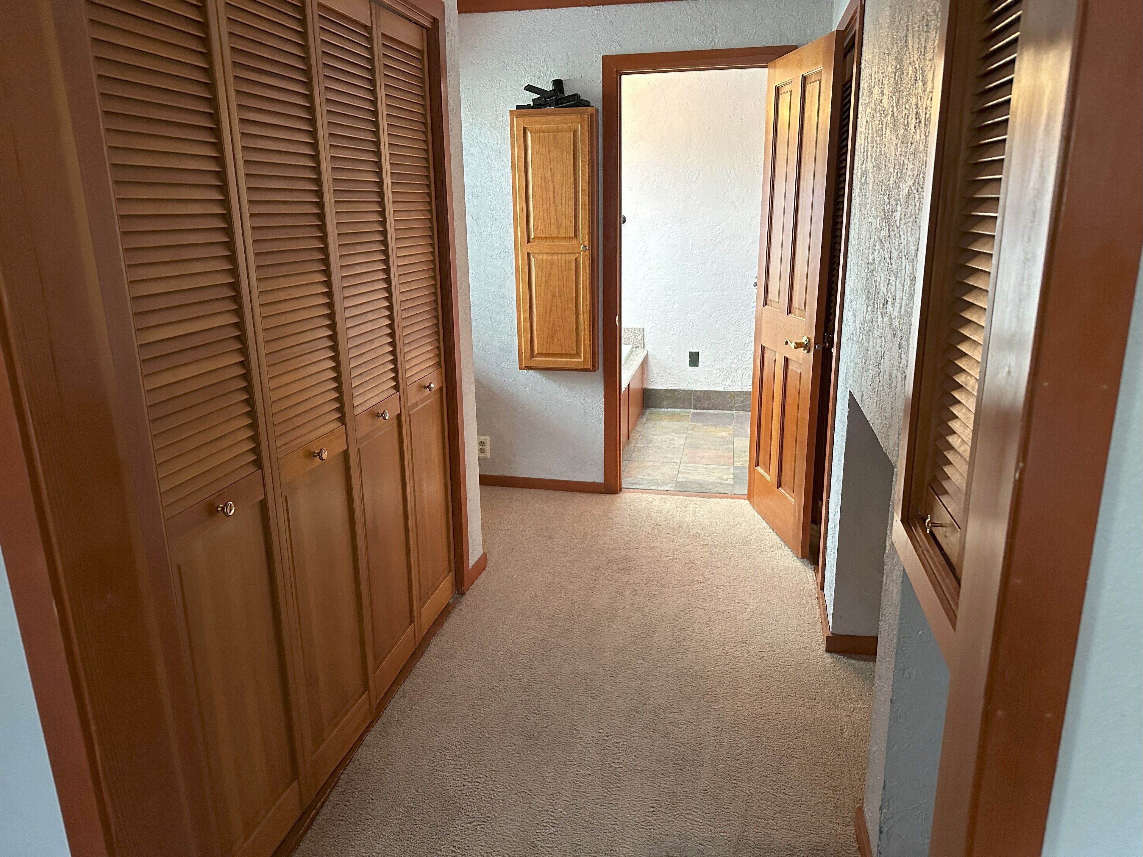 Un couloir avec des placards en bois et une porte donnant accès à une salle de bain.