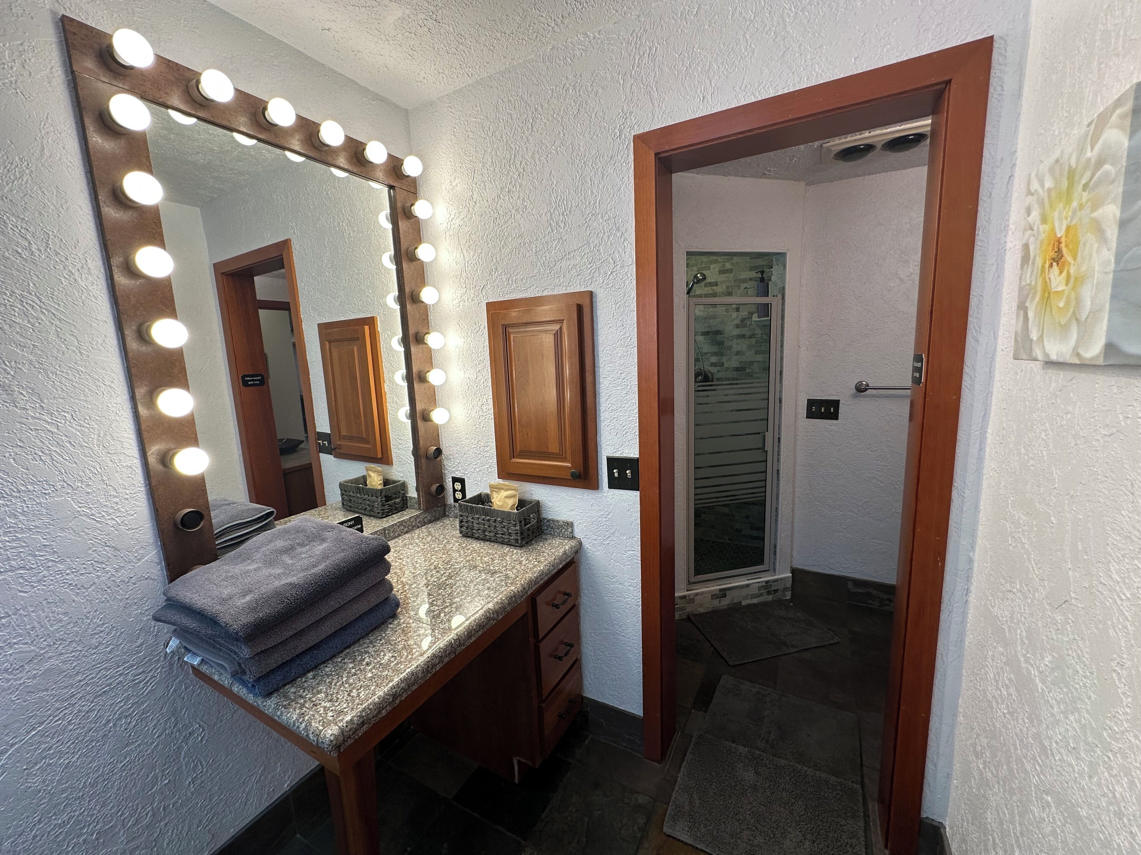 Une salle de bain avec un meuble-lavabo, un miroir avec éclairage intégré, un porte-serviettes et une porte de douche.