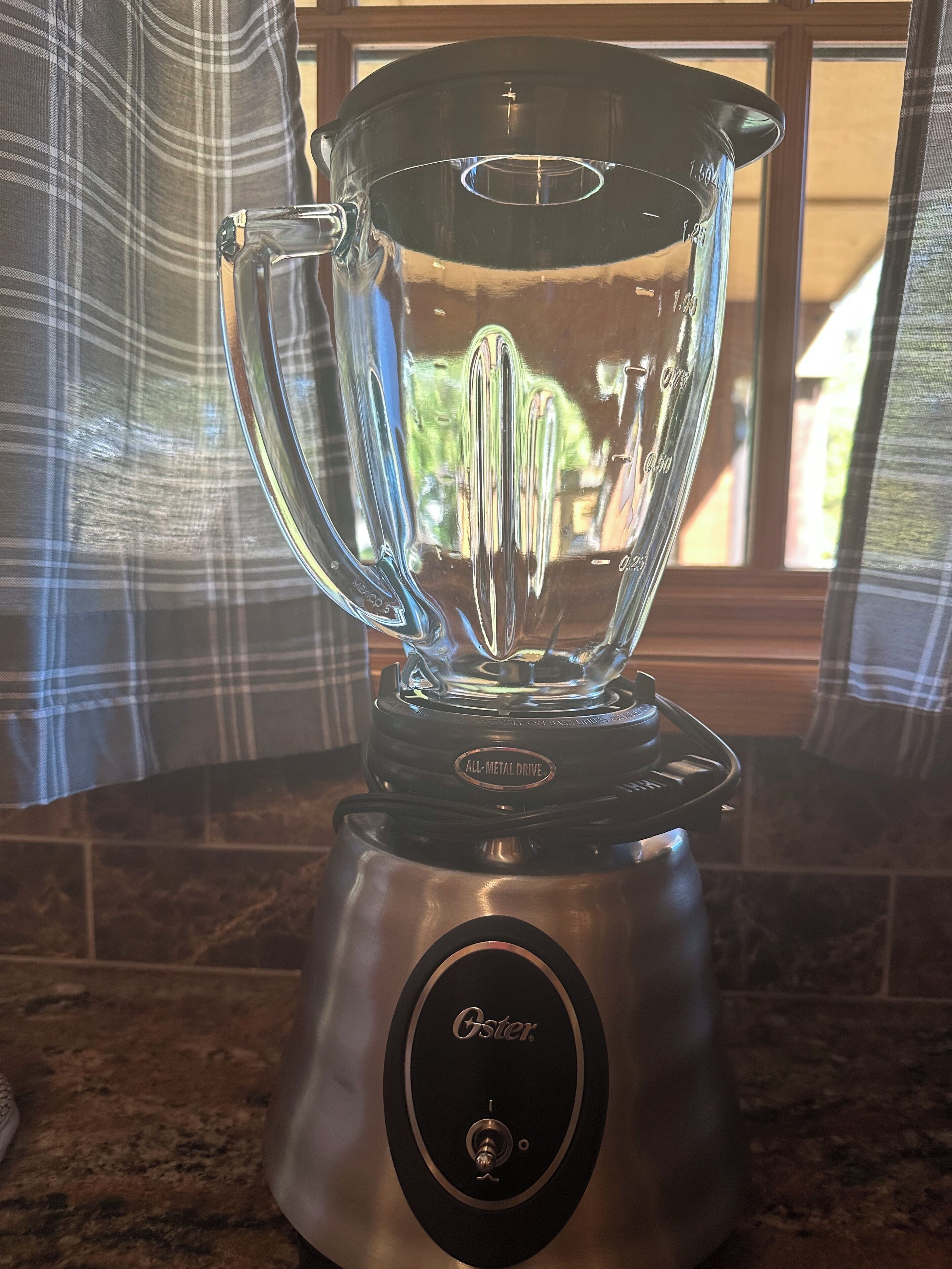 A kitchen with a stainless steel Oster blender on a granite countertop.
