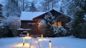 Une cabane en bois dont le toit est recouvert de neige, avec un sentier menant à l’entrée.