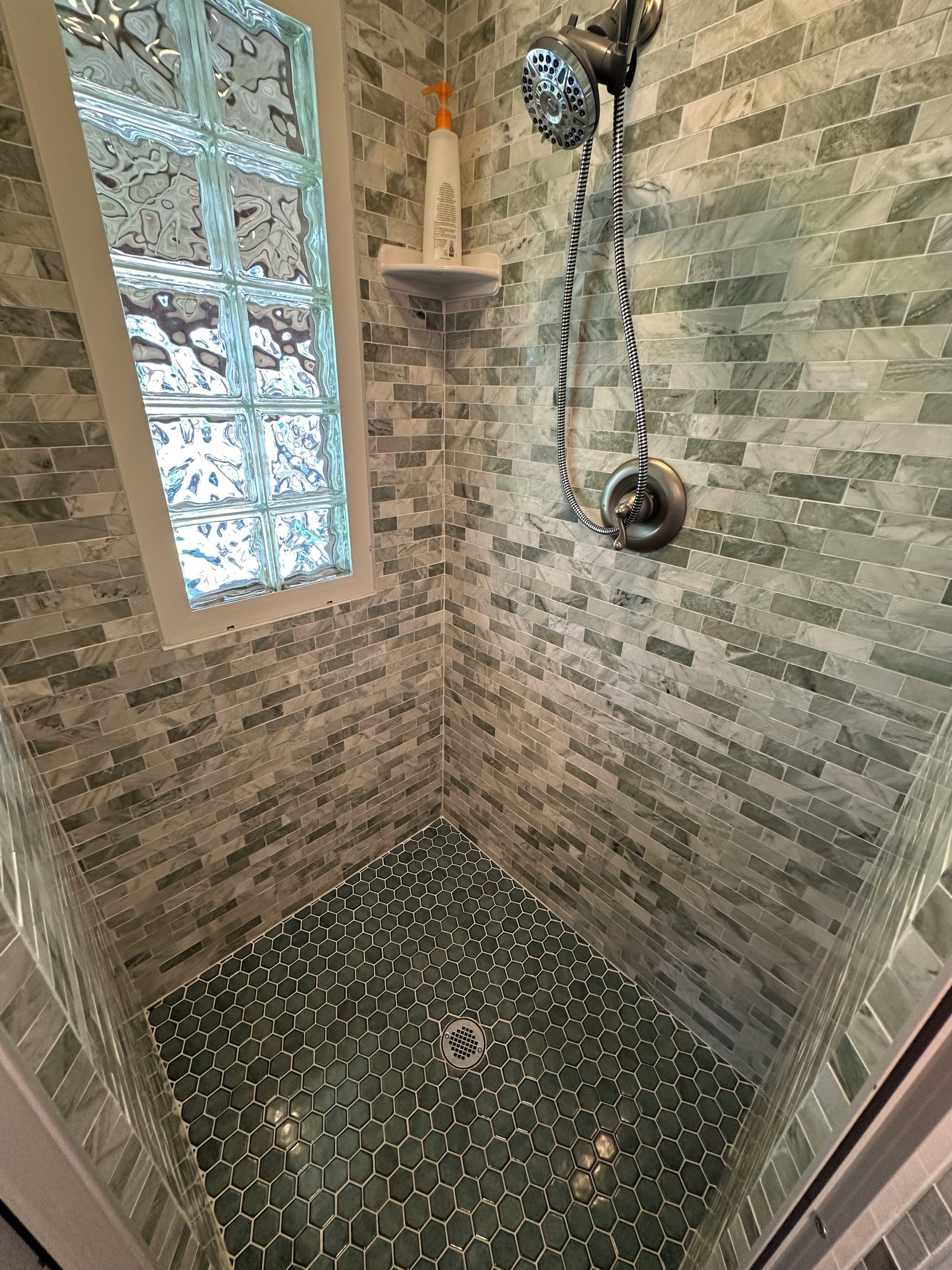 A shower with a glass door, a handheld showerhead, and a soap dispenser on a shelf.