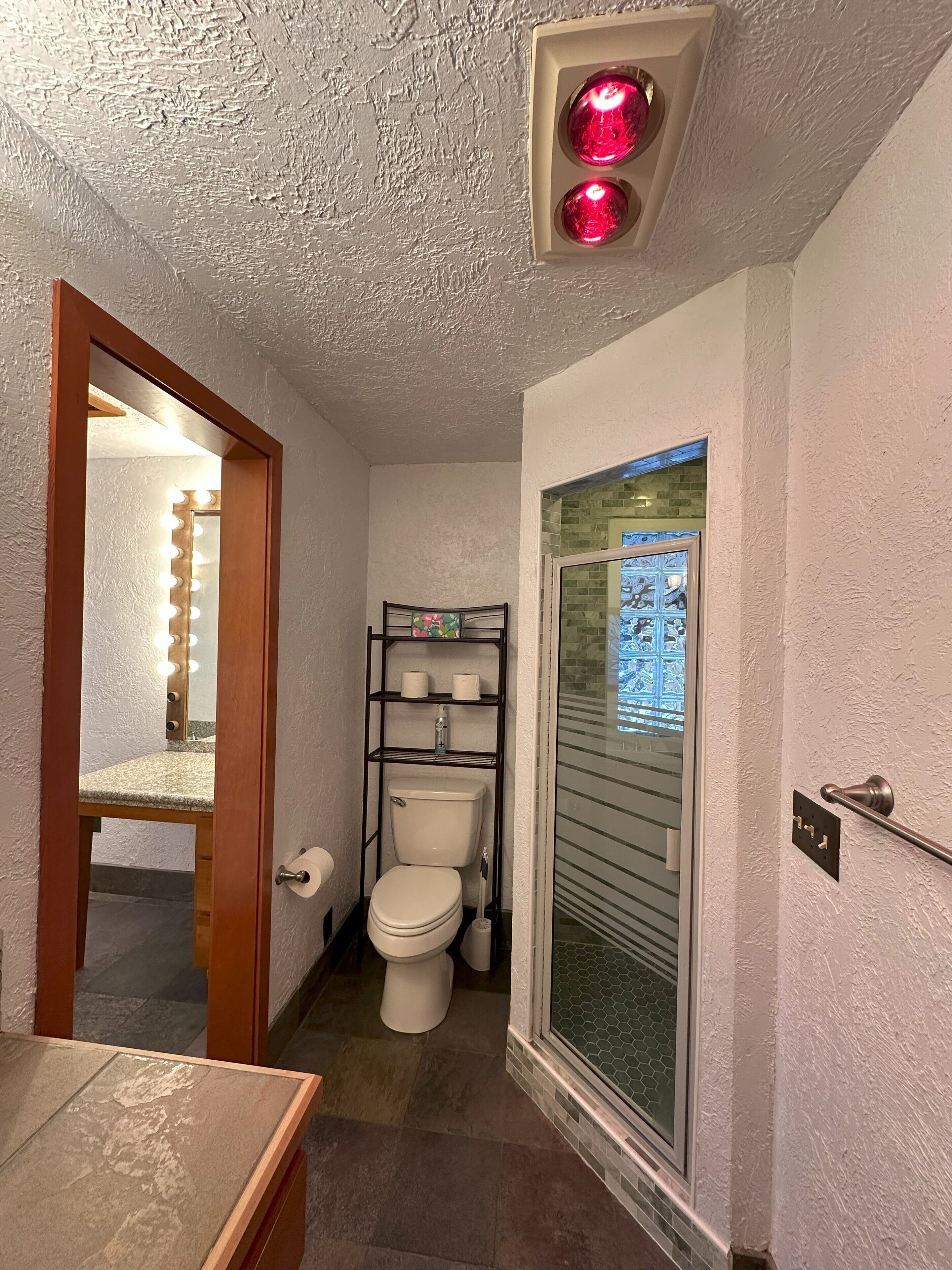 Ein Badezimmer mit Toilette, Ablagefläche für Toilettenartikel, einem beleuchteten Spiegel und einem Fenster mit Blick.