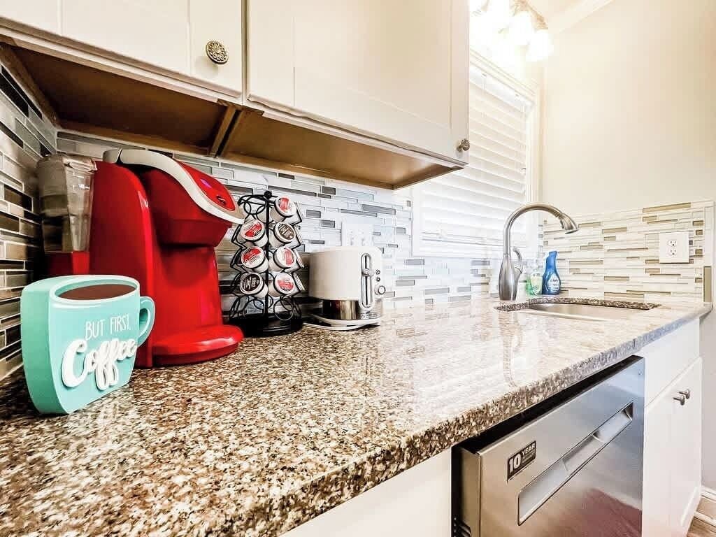 A kitchen with a granite countertop, a coffee maker, a mug, and a dishwasher.