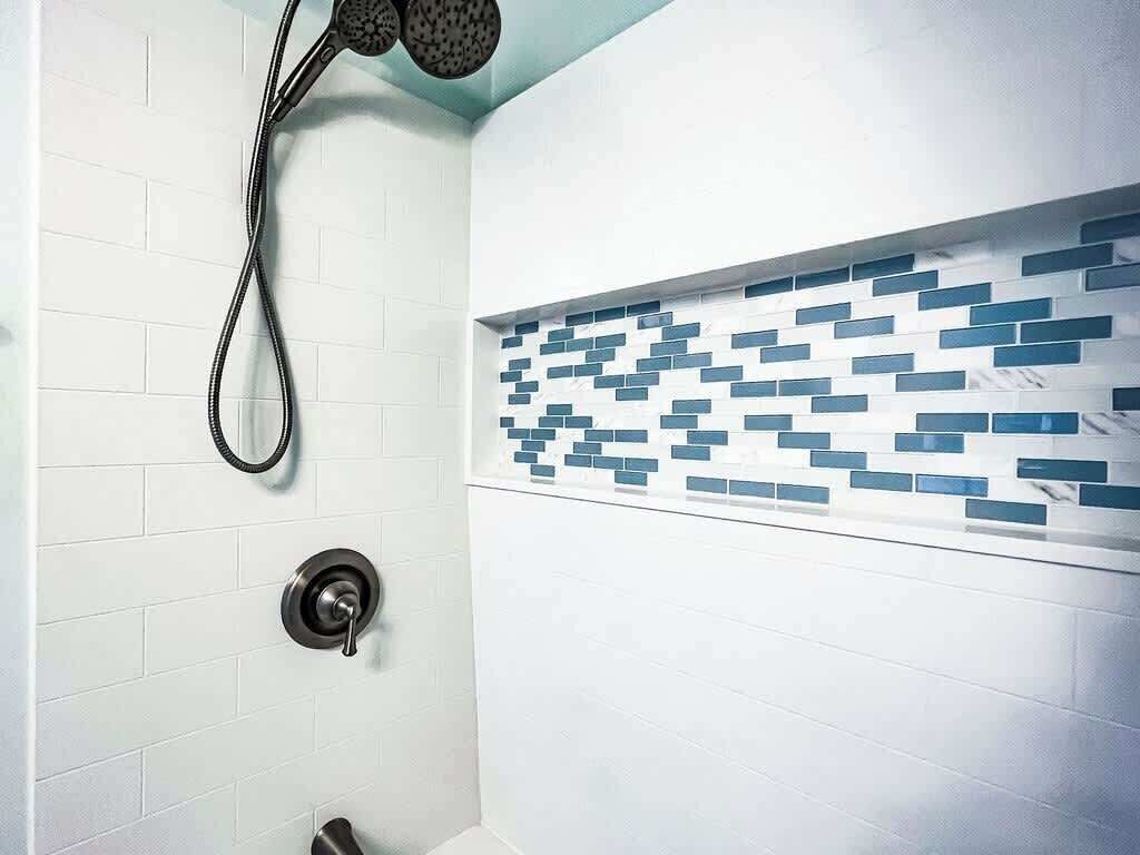 Een badkamer met witte betegelde wanden, een douche met handdouche en een decoratief blauw-wit tegelpatroon op de muur.