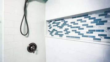 Een badkamer met witte betegelde wanden, een douche met handdouche en een decoratief blauw-wit tegelpatroon op de muur.