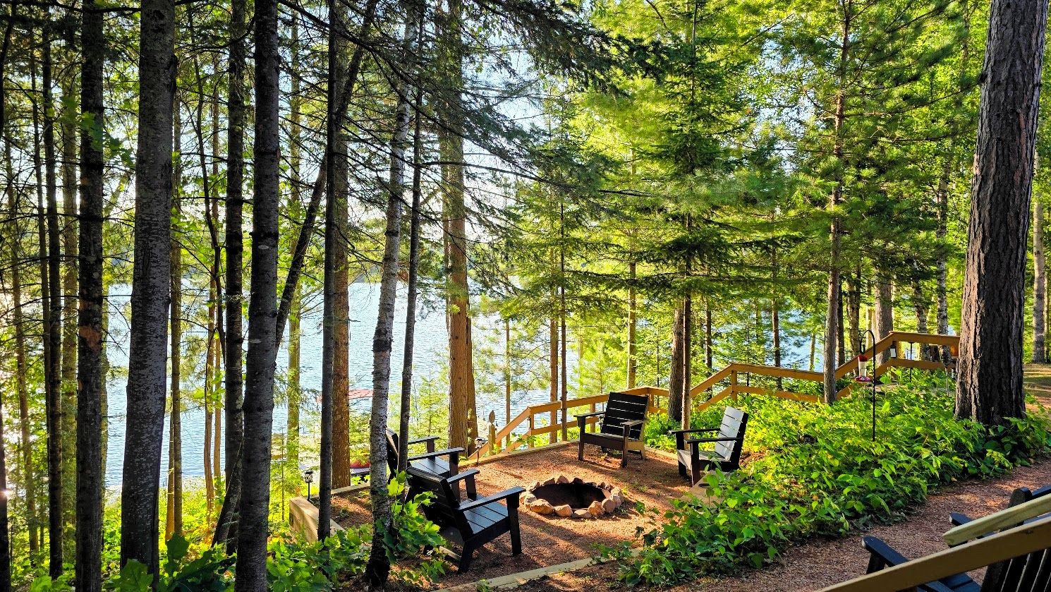 Un espace boisé doté d’une terrasse en bois, de bancs et d’un foyer.
