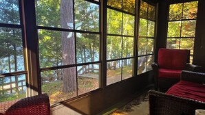 Een kamer met grote ramen, rieten meubels en uitzicht op bomen.