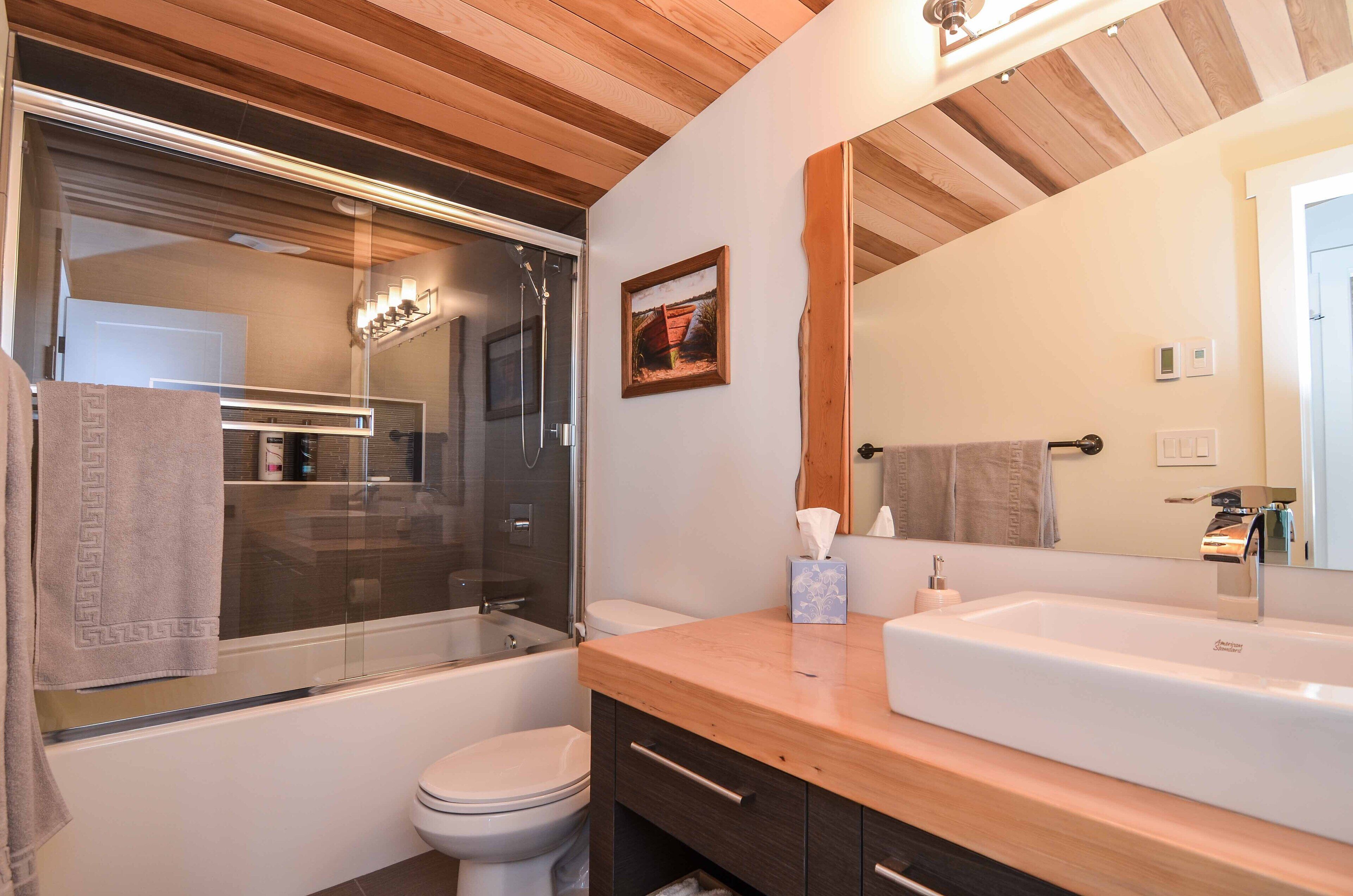 Une salle de bain moderne avec un plafond en bois, une cabine de douche en verre, un lavabo blanc et un grand miroir.
