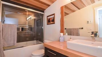 Une salle de bain moderne avec un plafond en bois, une cabine de douche en verre, un lavabo blanc et un grand miroir.