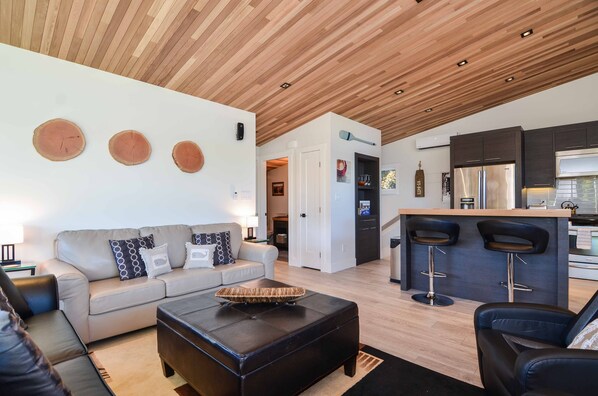 A modern living room with a sofa, ottoman, and a wooden ceiling.