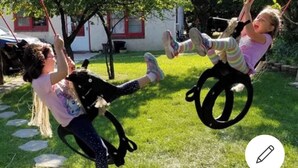 Due bambini si divertono sull’altalena in un giardino con una casa sullo sfondo.