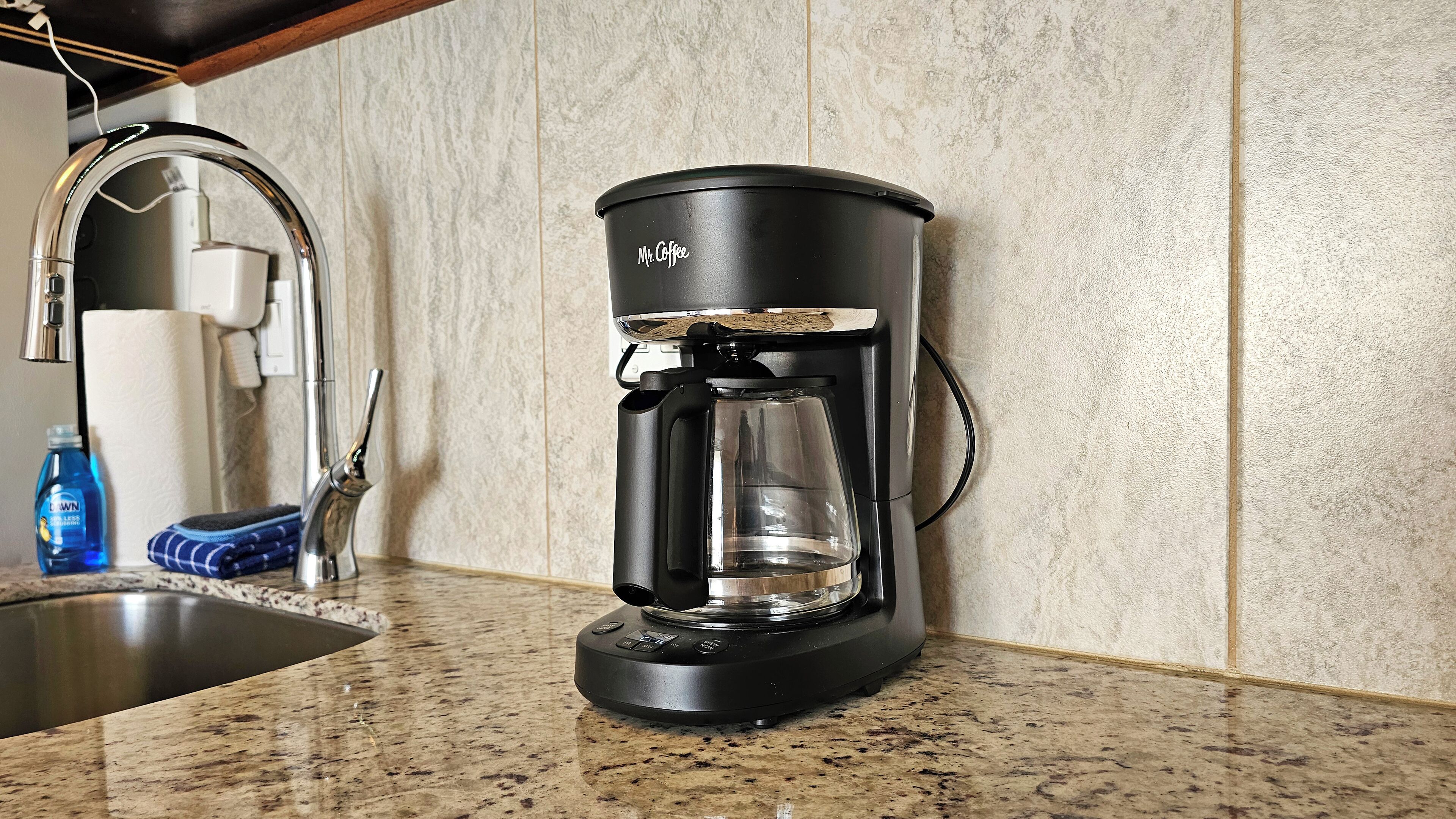 Eine Kaffeemaschine auf einer Granitarbeitsplatte mit einem Edelstahlarmaturen und einem Handtuchspender im Hintergrund.