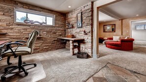 A room with a stone wall, a desk, a red sofa, and a window.