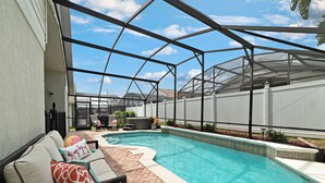 Une piscine extérieure couverte, dotée d’un patio, d’un barbecue et d’un espace détente avec des coussins.