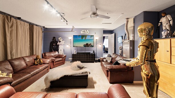 Un salon moderne avec des canapés en cuir, un téléviseur à écran plat et des objets de collection sur le thème de Star Wars.