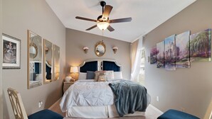 Une chambre à coucher comprenant un lit, deux chaises, un ventilateur de plafond et des œuvres d’art accrochées au mur.