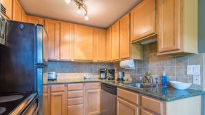 A kitchen with wooden cabinets, a black refrigerator, a coffee maker, a sink, and a dish rack.